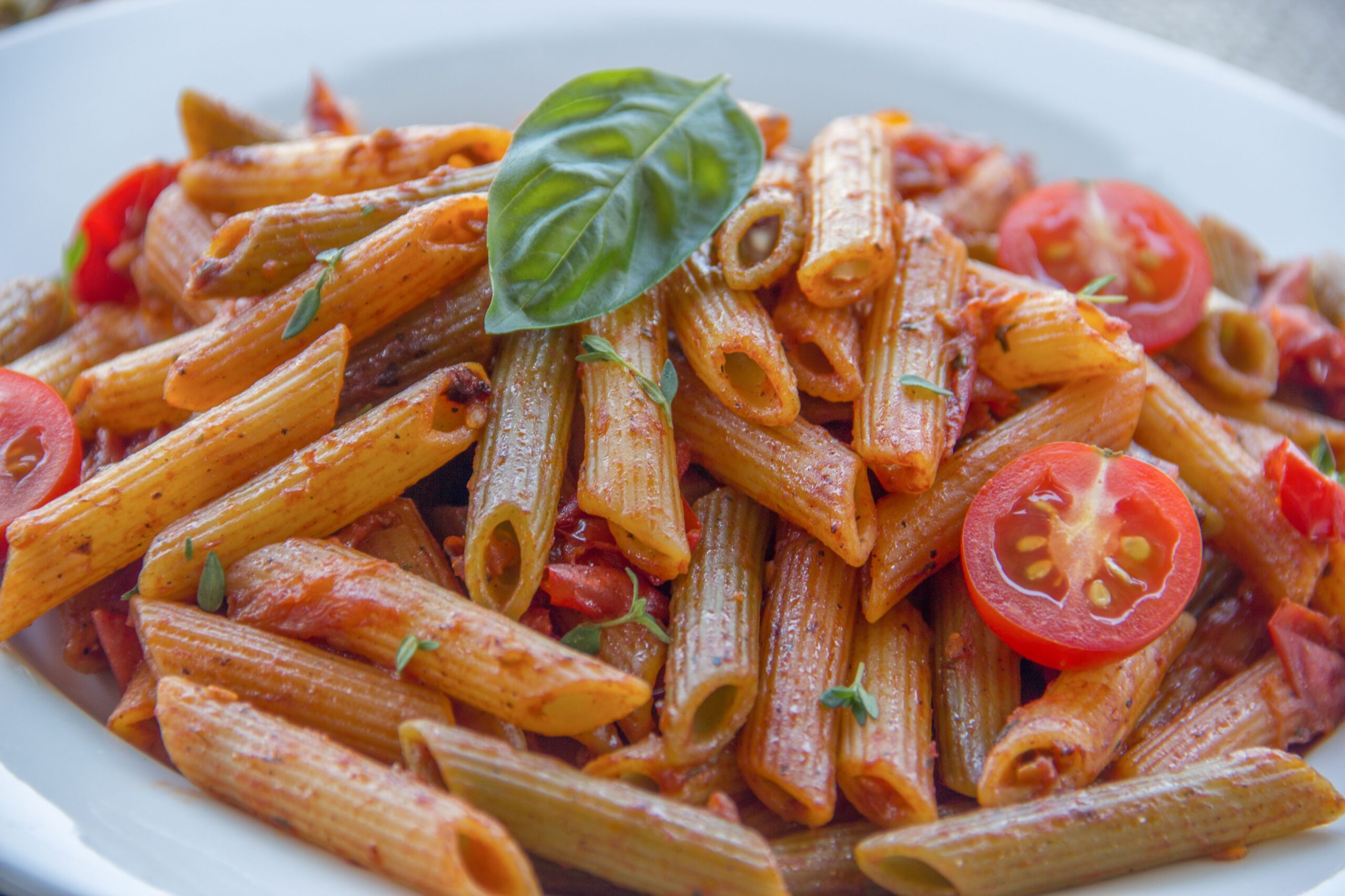 Al dente penne pasta coated in rich crushed cherry tomato sauce garnished with fresh basil leaves and halved tomatoes