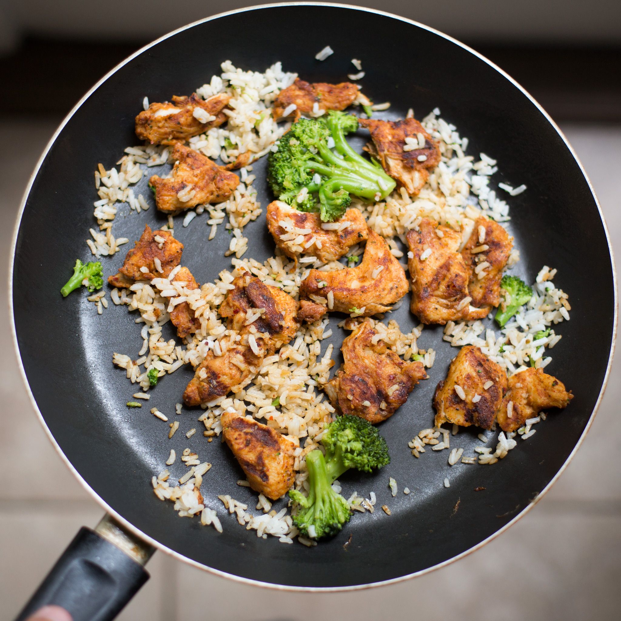Chicken pieces searing in a dark skillet pan alongside broccoli florets