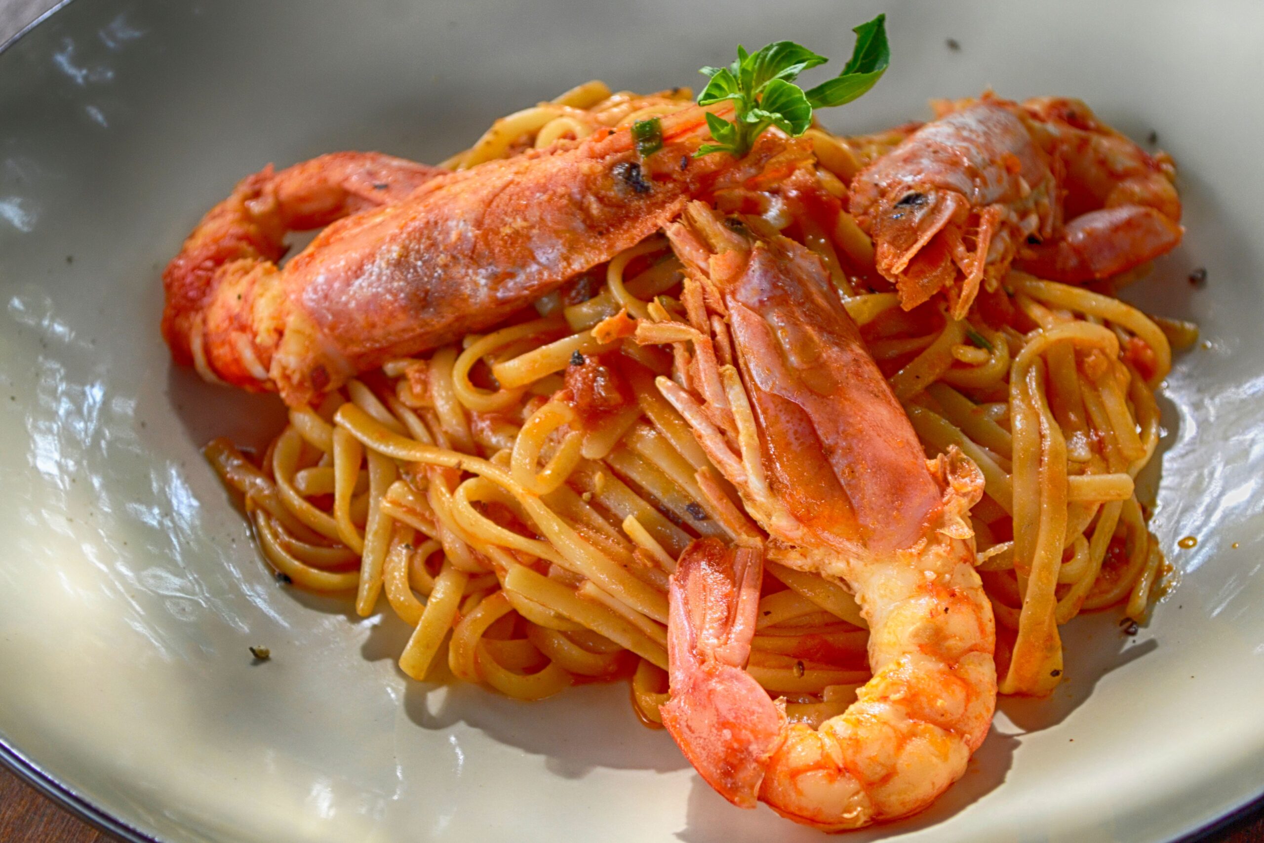 Rich red-tinged garlic shrimp pasta simmering with pan juices in a deep skillet dish