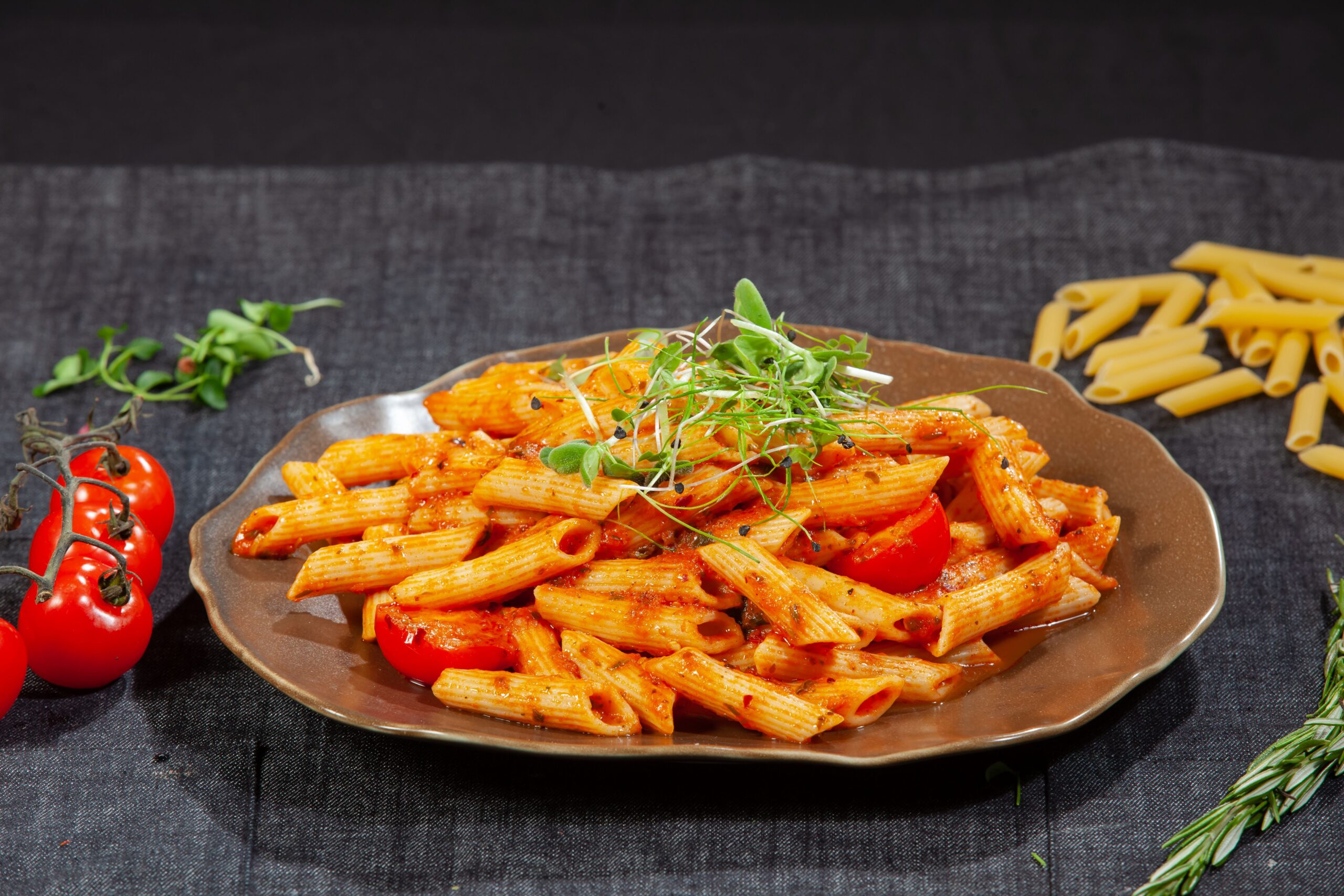 Rich tomato basil penne pasta served in a rustic earthen platter garnished with fresh greens