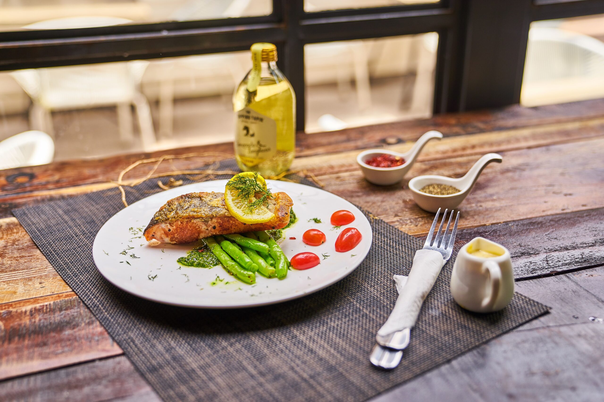 Elegantly plated salmon fillet topped with a lemon wheel over green beans and tomatoes on a rustic wooden table
