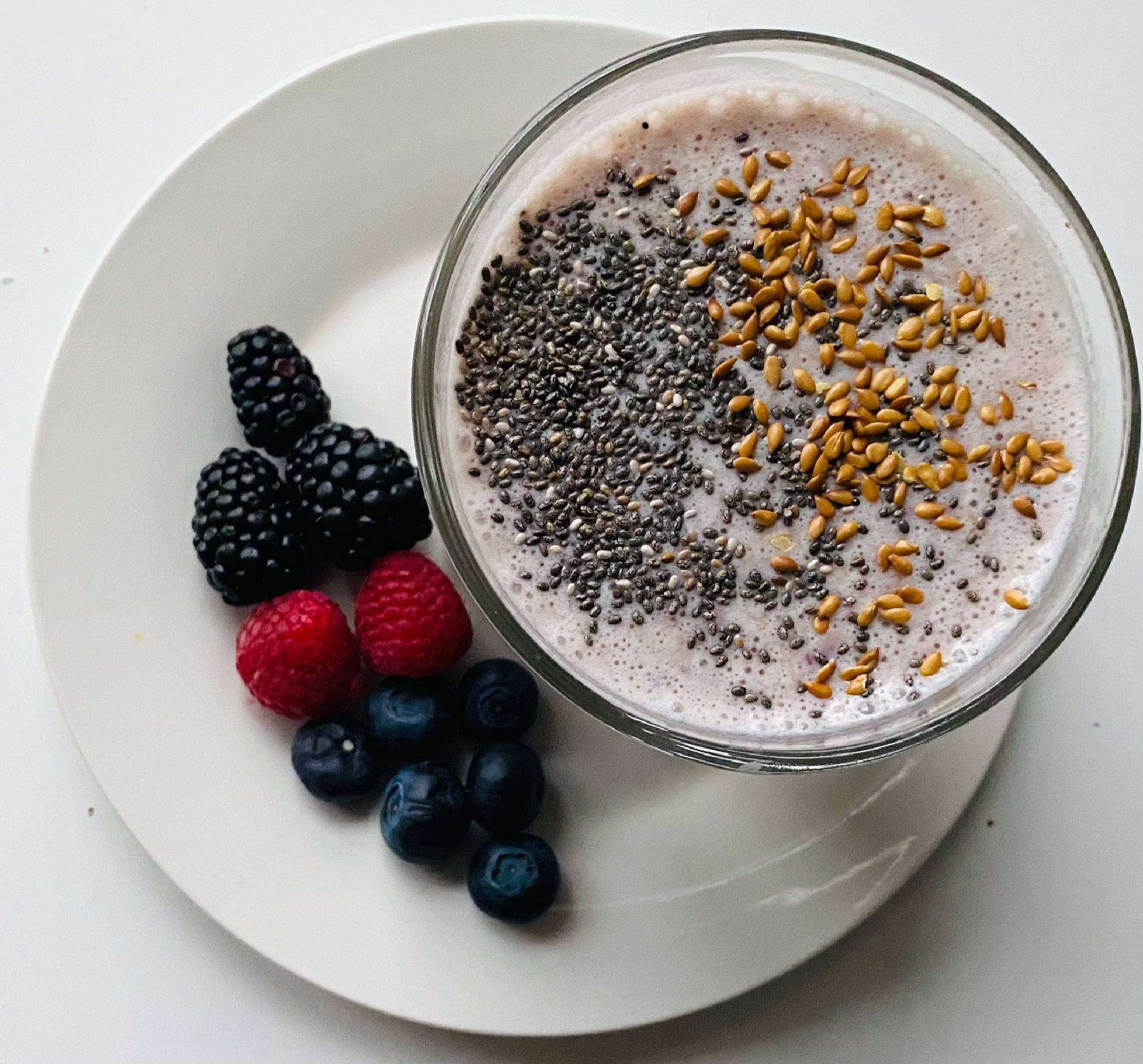 Thick green smoothie bowl topped with banana slices, chia seeds, and fresh berries in a wooden bowl