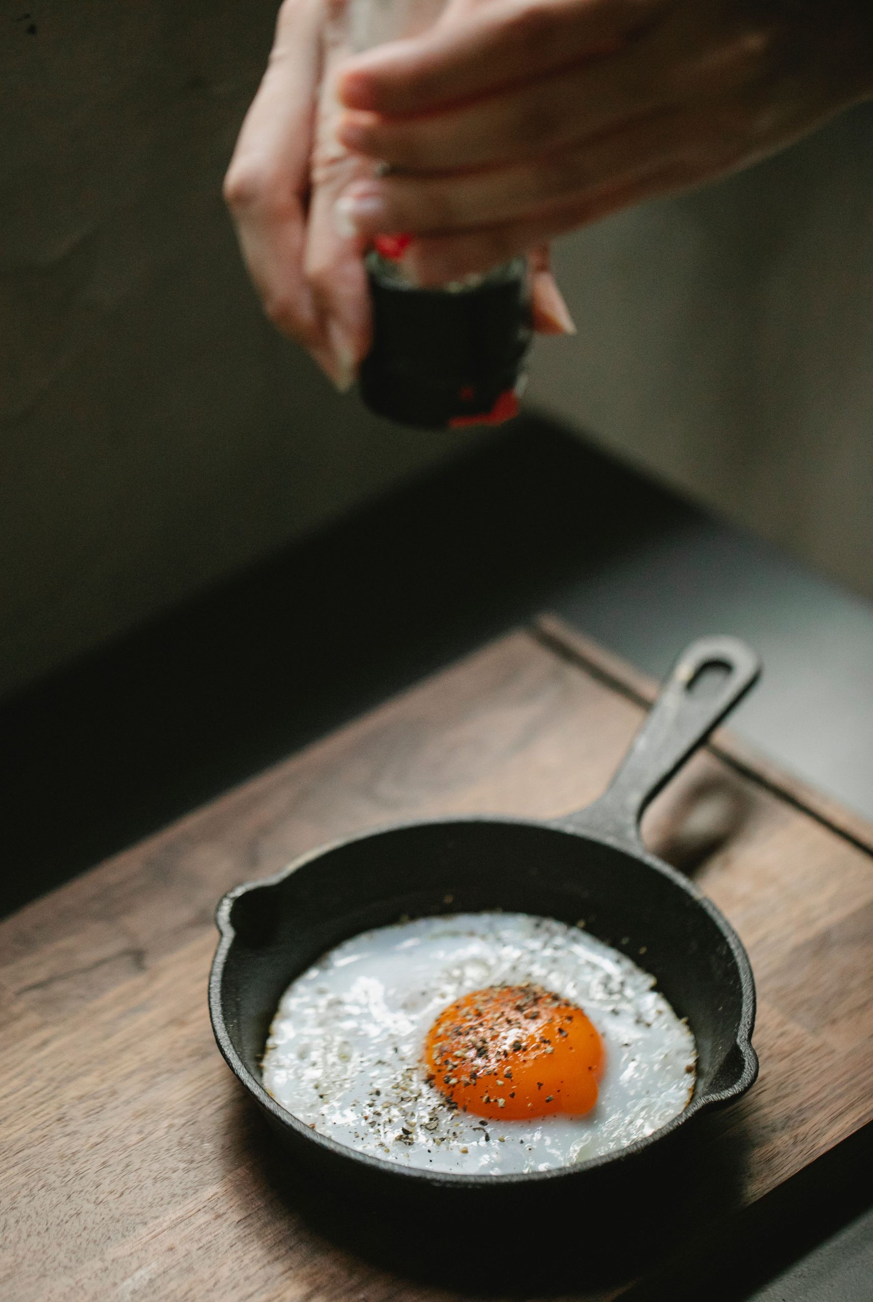 Adding freshly ground black pepper to an egg in a cast iron pan
