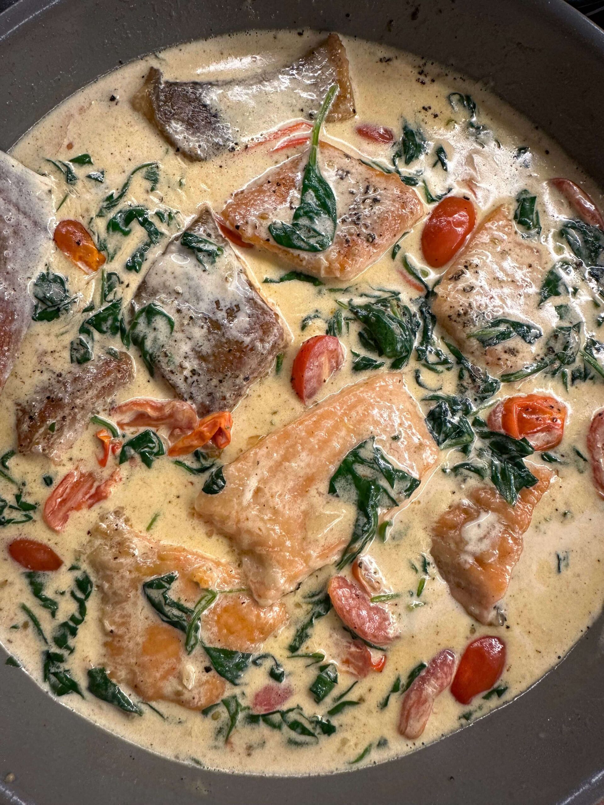 Creamy Tuscan garlic salmon in skillet with spinach and tomatoes