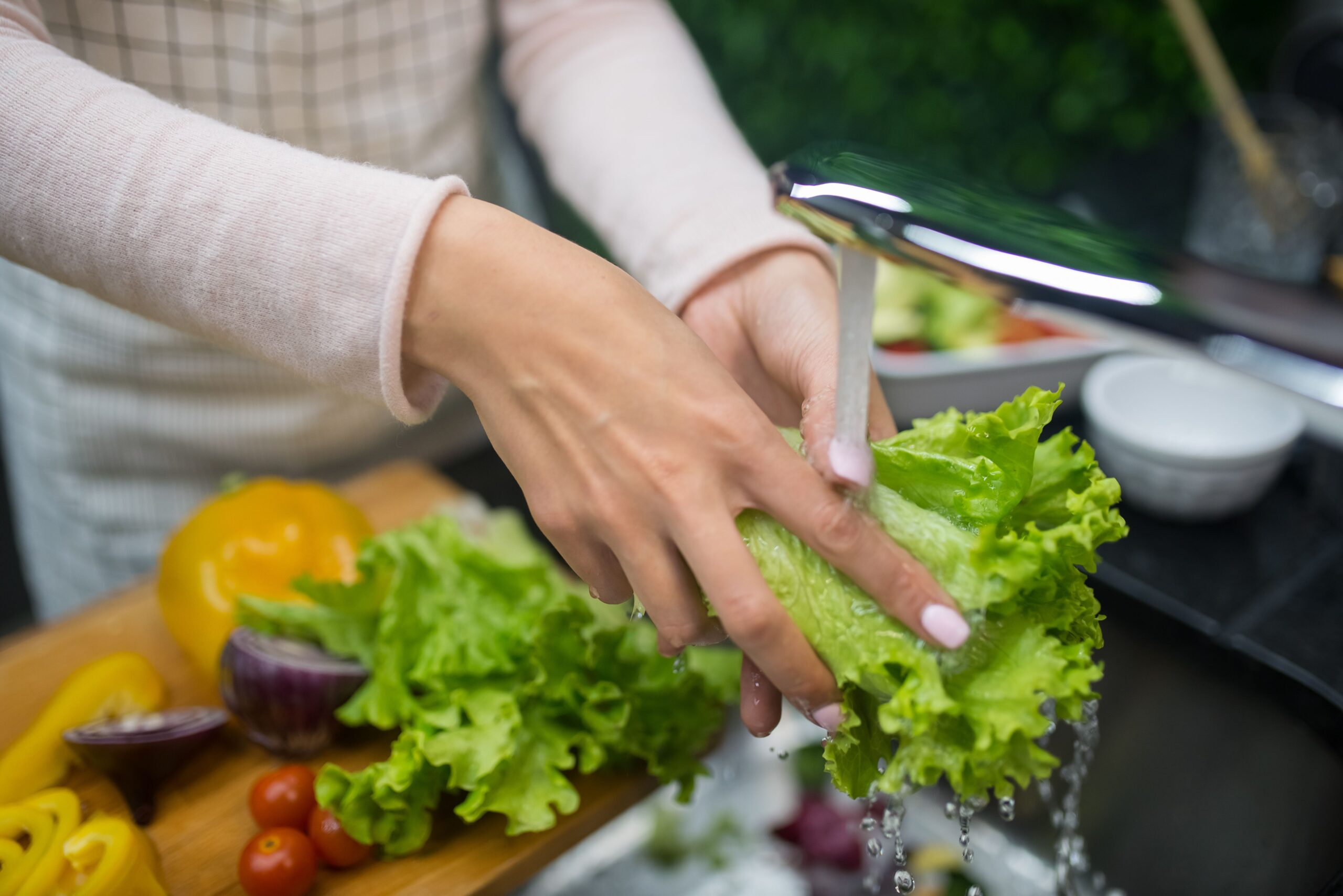 Washing fresh green lettuce leaves under running kitchen sink water