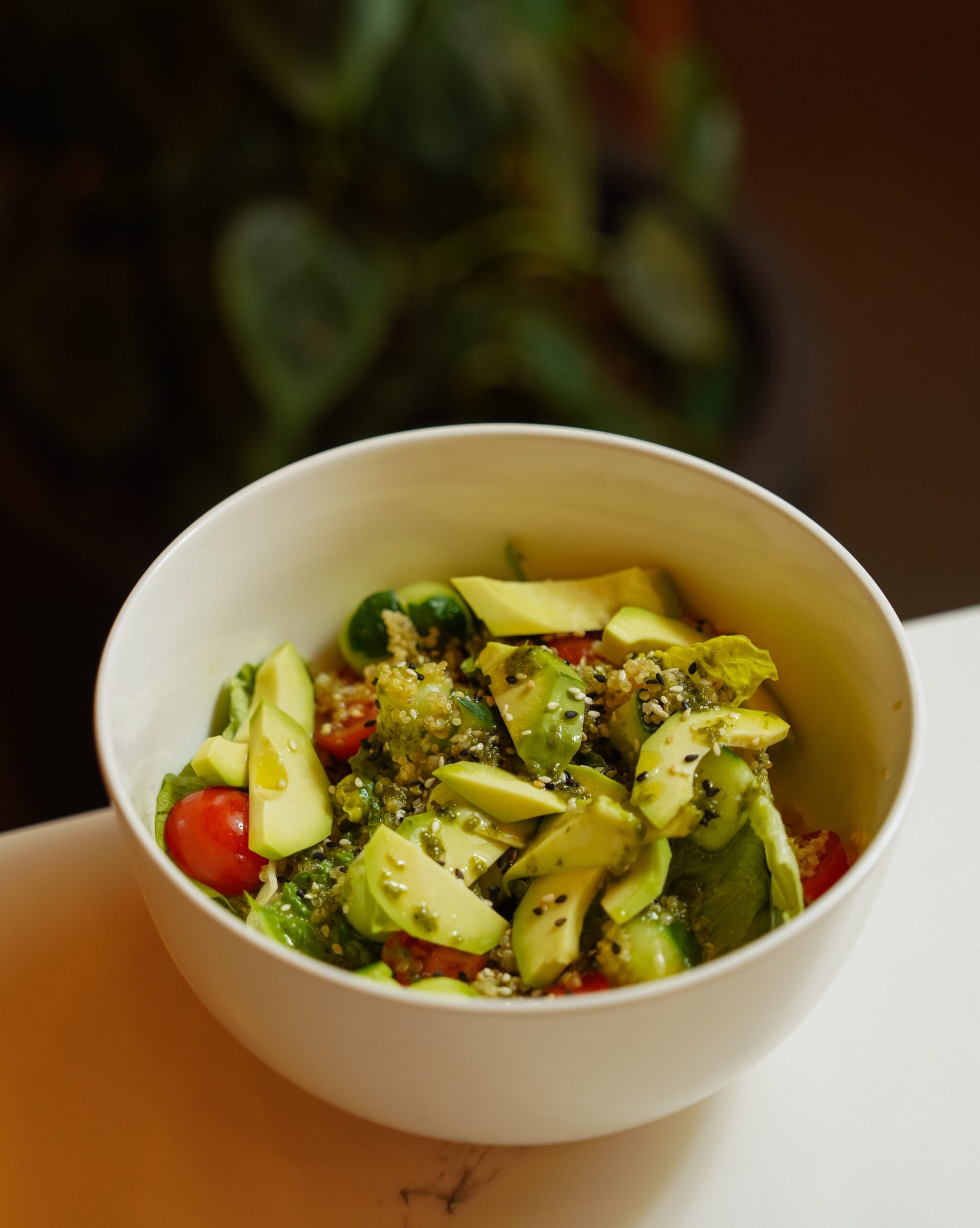 White ceramic bowl filled with fresh quinoa salad, diced avocado, cherry tomatoes, and sesame seeds