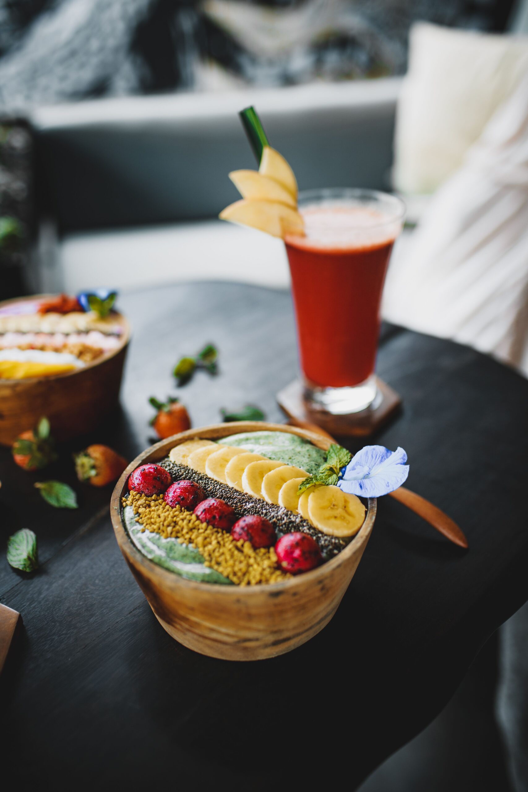 Thick green smoothie bowl topped with banana slices, chia seeds, and fresh berries in a wooden bowl