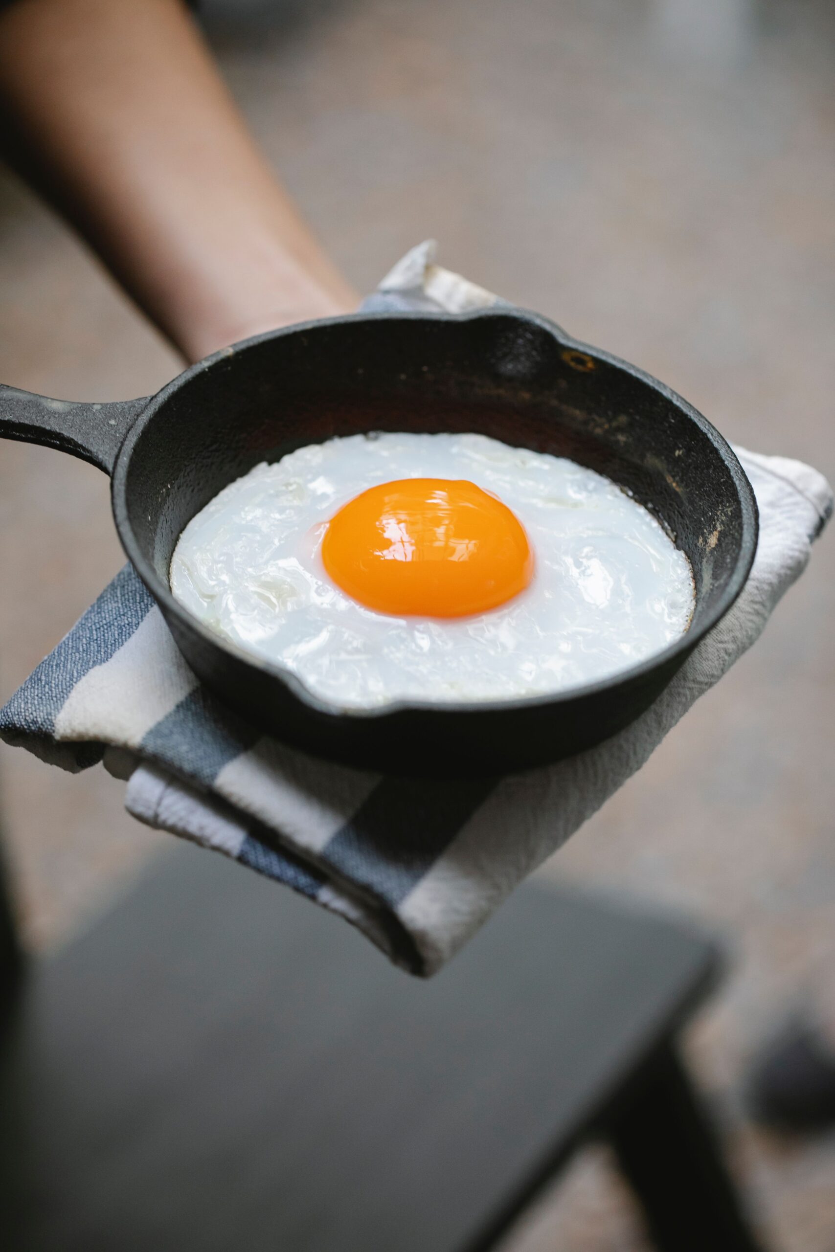 Perfect sunny-side up egg in a small cast iron skillet held with a kitchen towel
