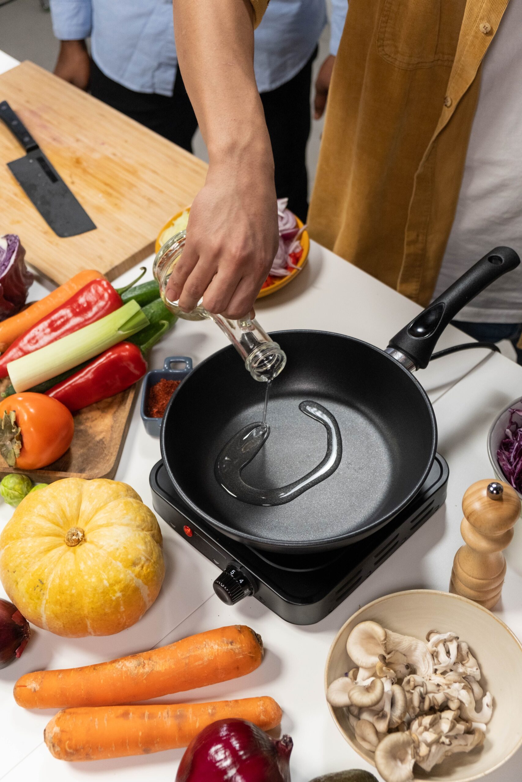 Pouring cooking oil into a nonstick frying pan surrounded by fresh vegetables
