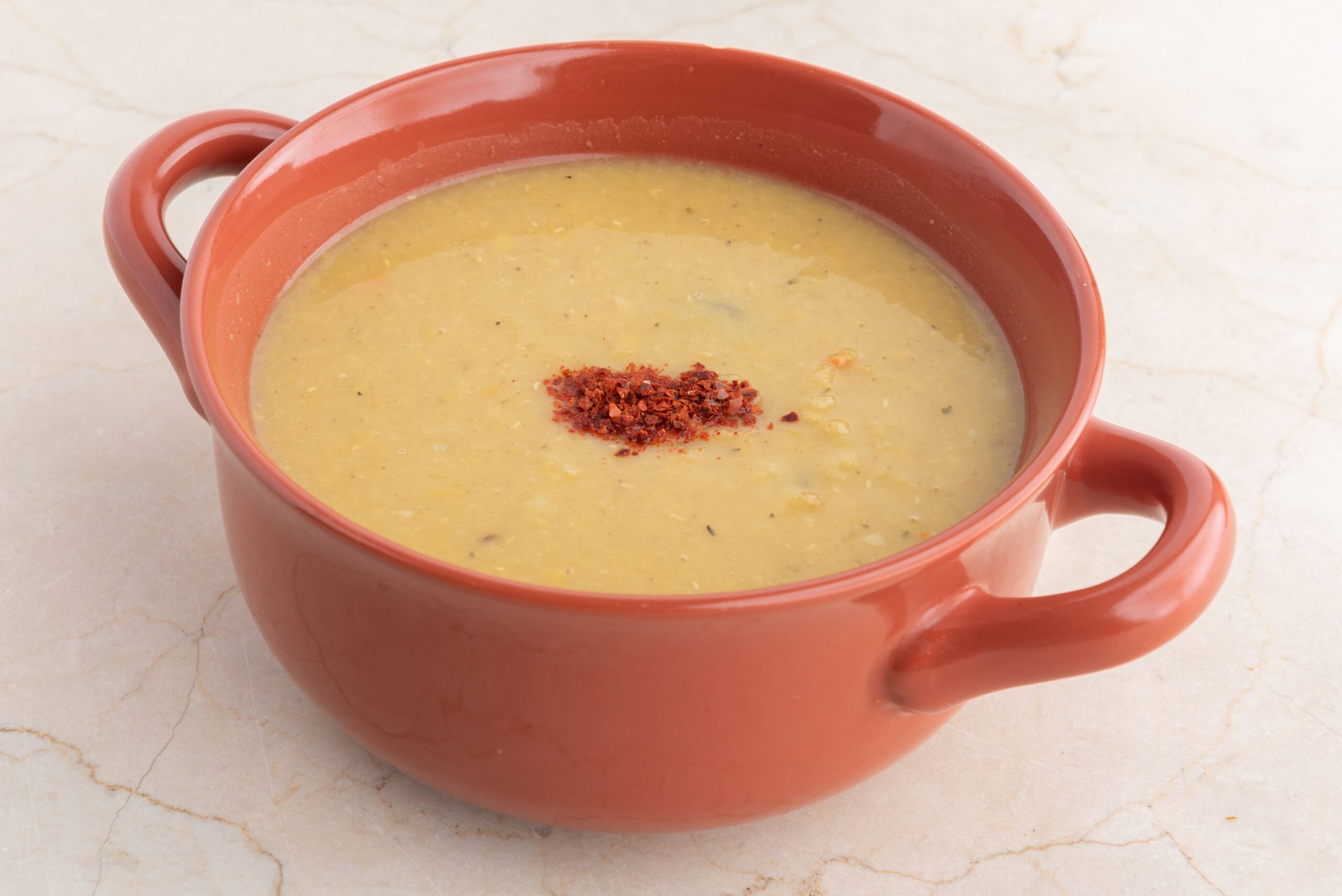 Warm yellow spiced lentil soup served in a rustic clay bowl topped with chili flakes