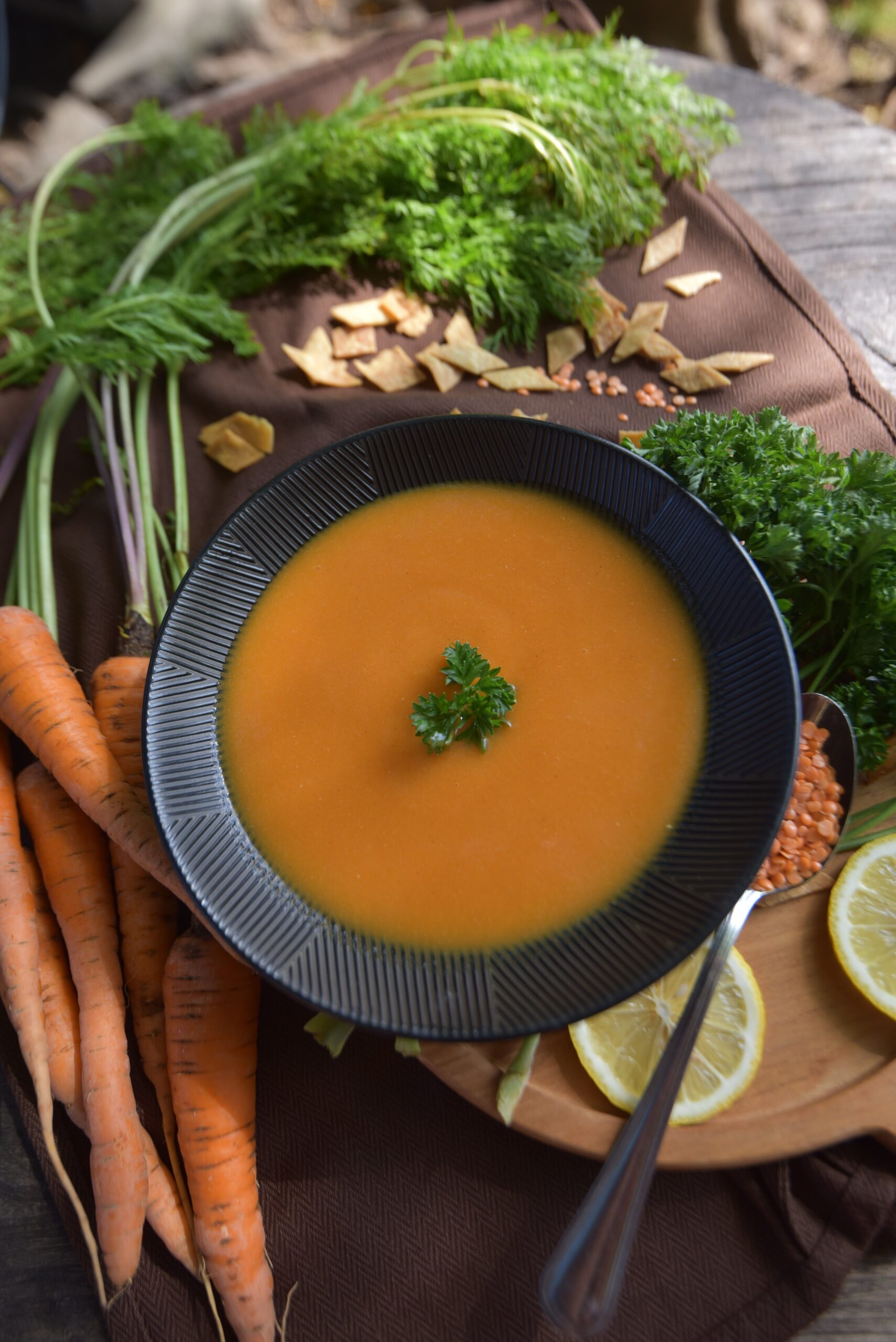 Creamy blended red lentil soup garnished with fresh parsley and lemon slices in a black bowl