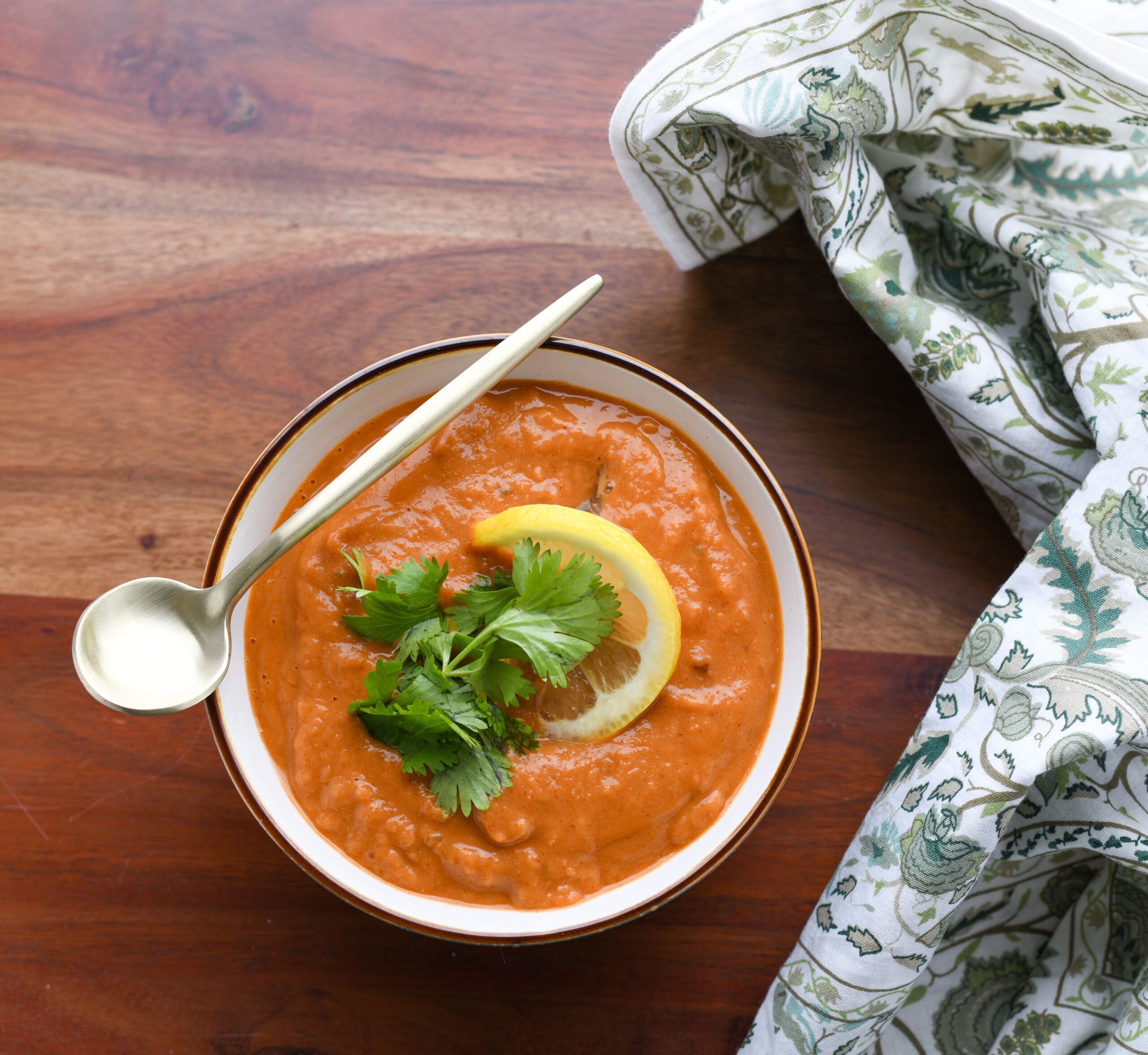 Creamy blended red lentil soup garnished with fresh parsley and lemon slices in a black bowl