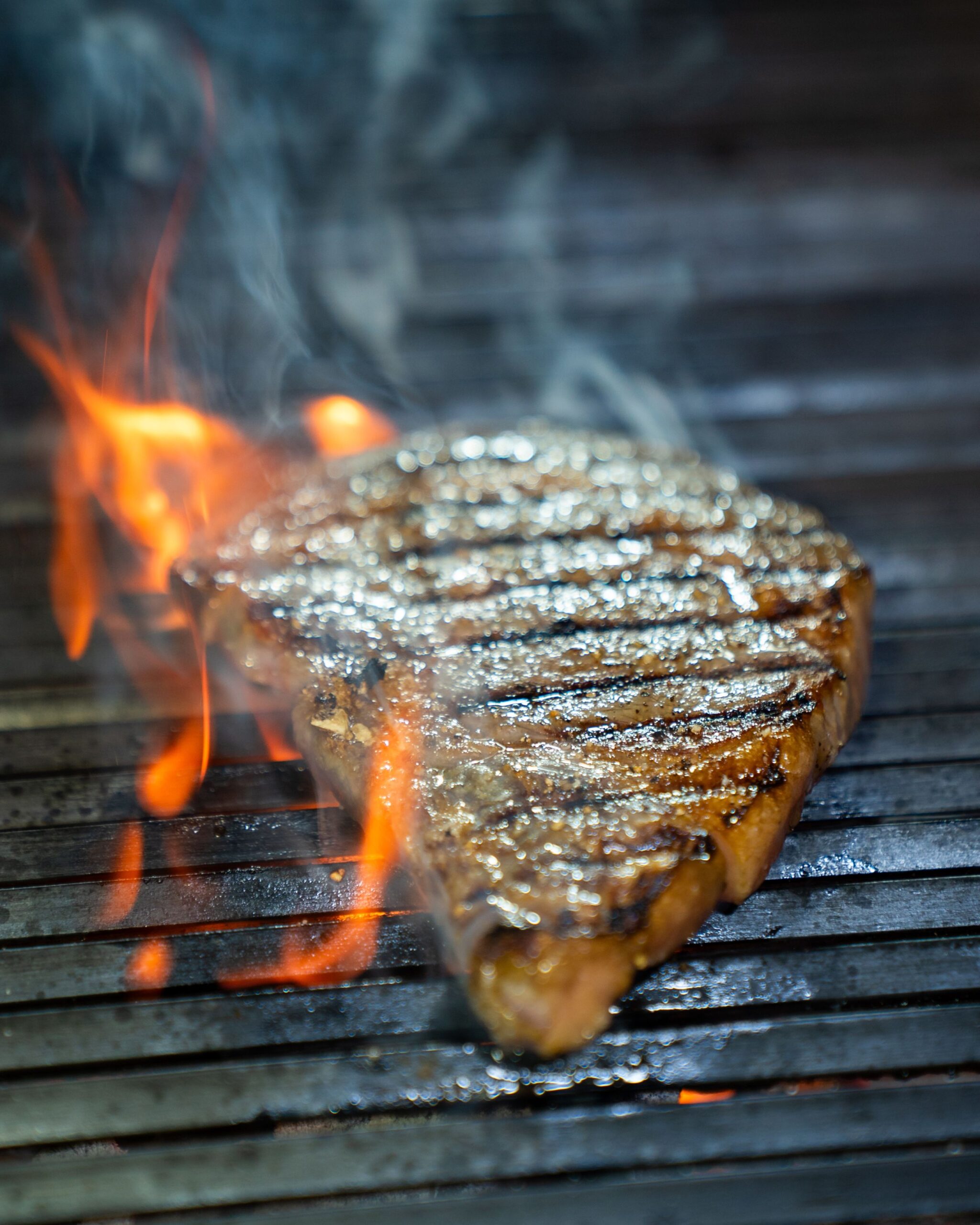 Juicy beef steak grilling over open flame grates with high heat flare-ups