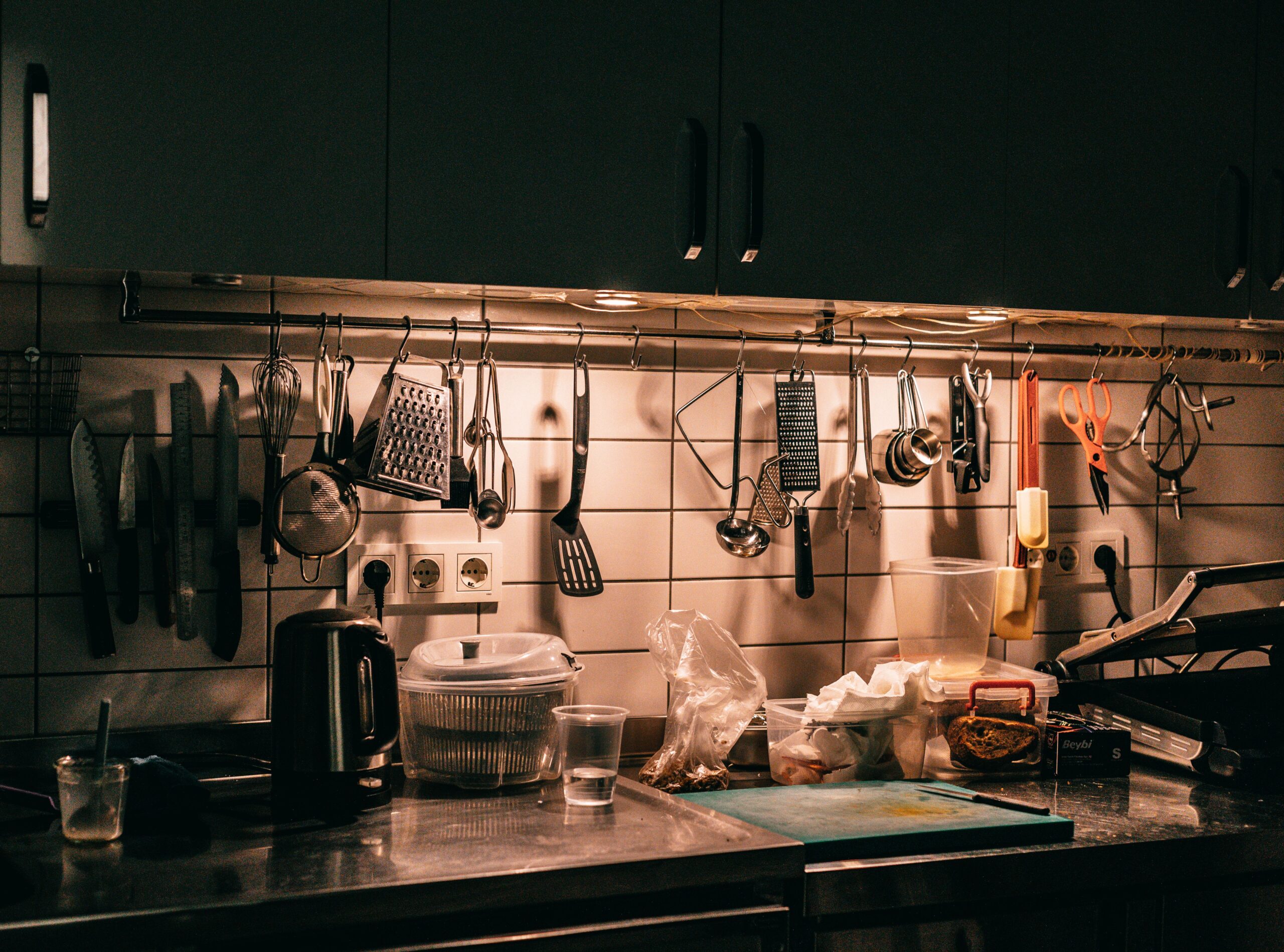 Busy culinary workstation with hanging stainless steel utensils and prep containers under warm light